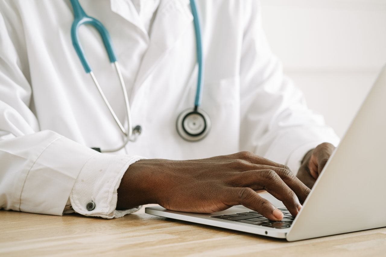 services-01 Close-up of a doctor using a laptop, wearing a stethoscope and white coat.