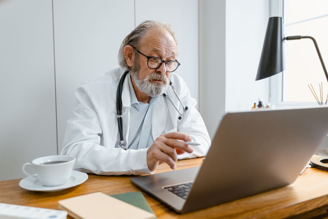 services-02 Senior male doctor using laptop for telehealth consultation in office setting.
